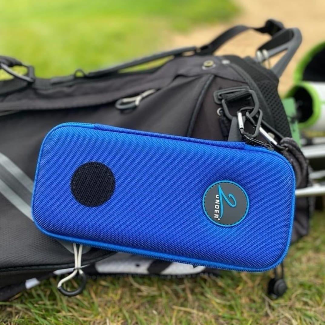 A 2Under Golf blue glove case securely clipped onto a black golf bag, showcasing its stylish design and convenient storage for premium golf gloves on the course.