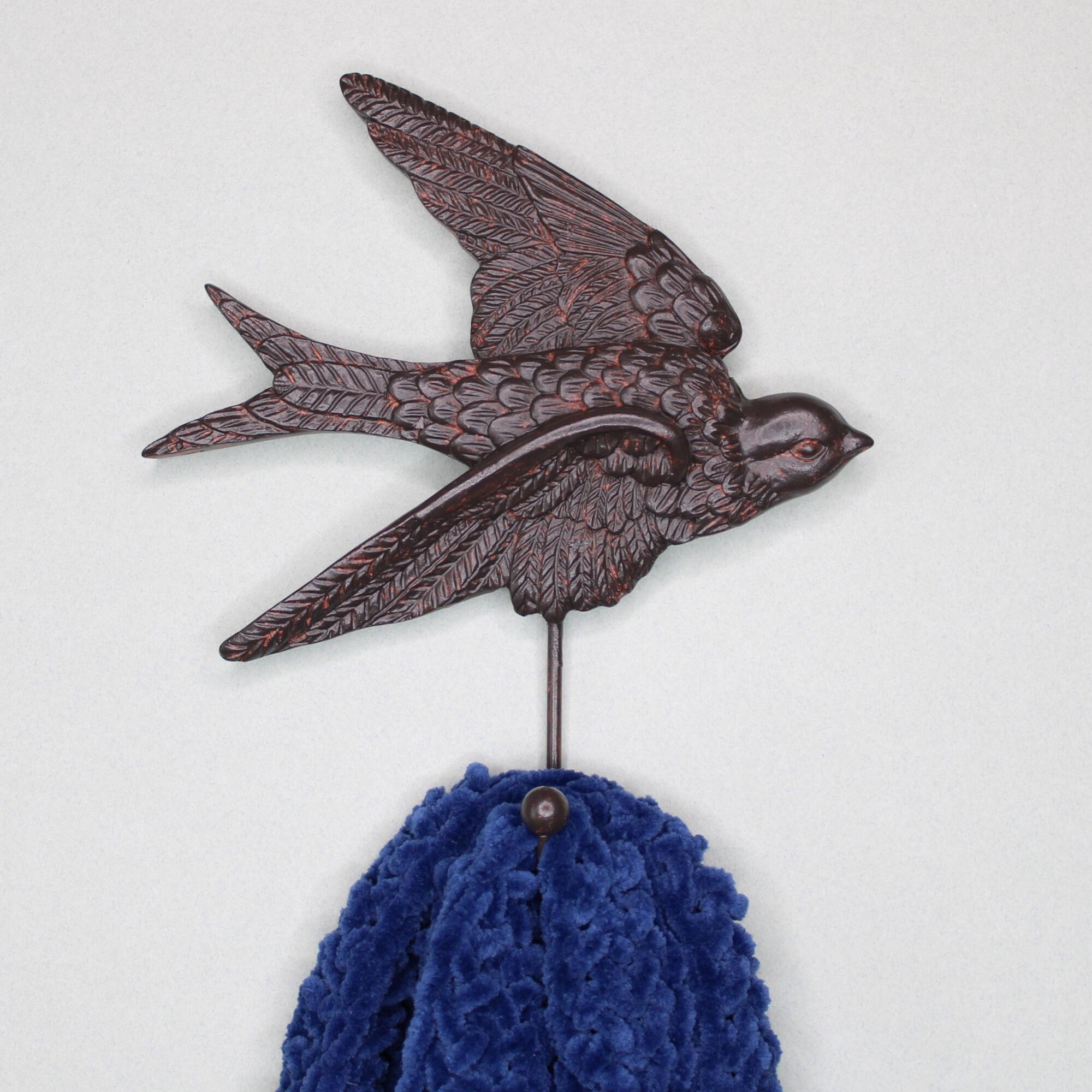 Swallow wall hook used to hang a dark blue knit scarf against a neutral background.