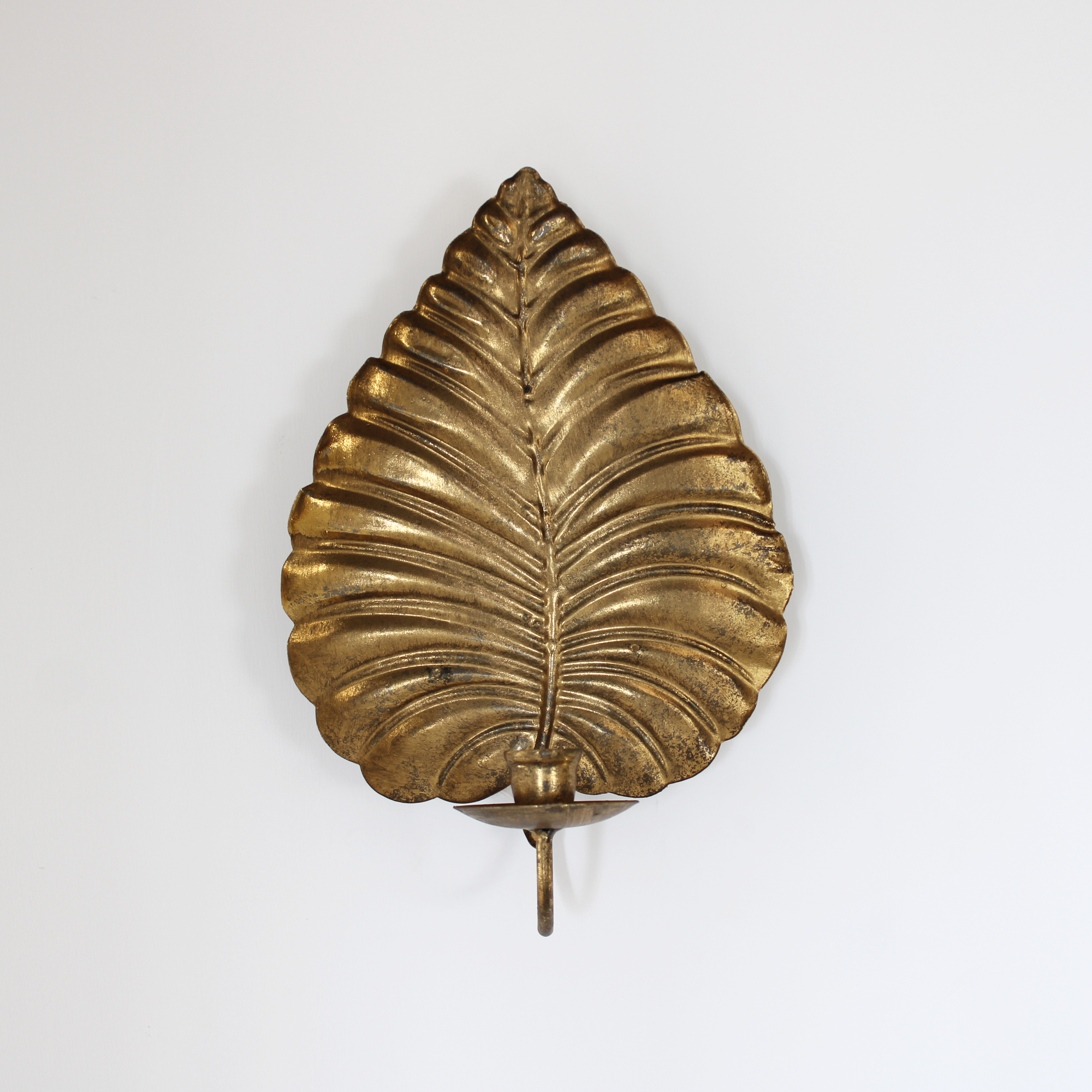 Rustic gold metal wall sconce in the shape of a large leaf, designed to hold a single candle.