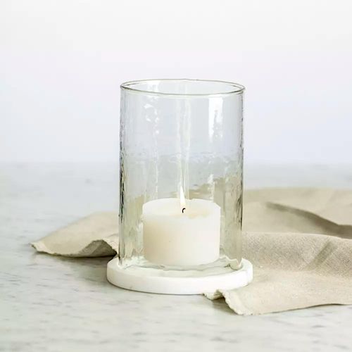 Hand-blown hammered glass hurricane lantern with a solid white marble base and a white pillar candle lit inside.