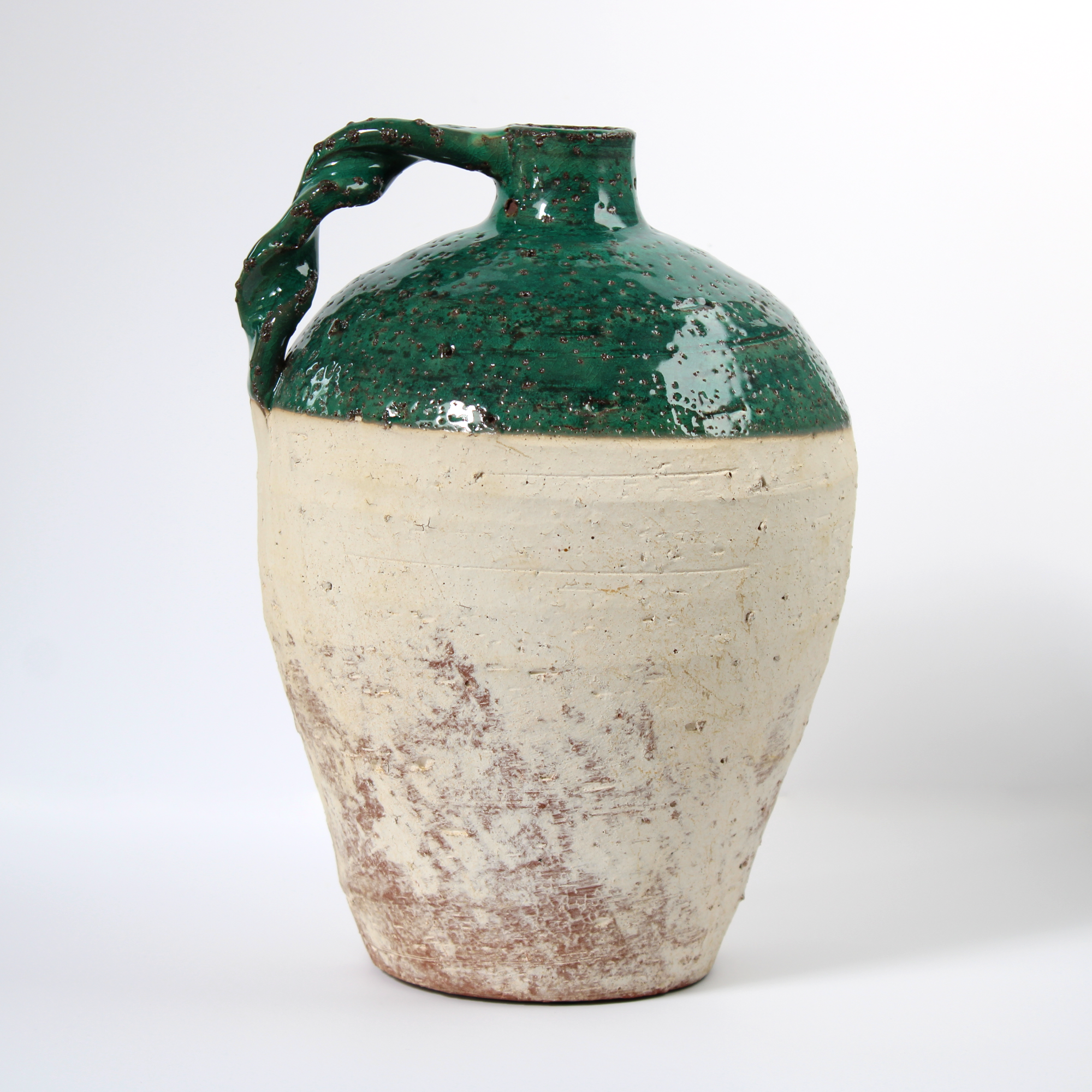 rustic terracotta jug with green glaze, side view.
