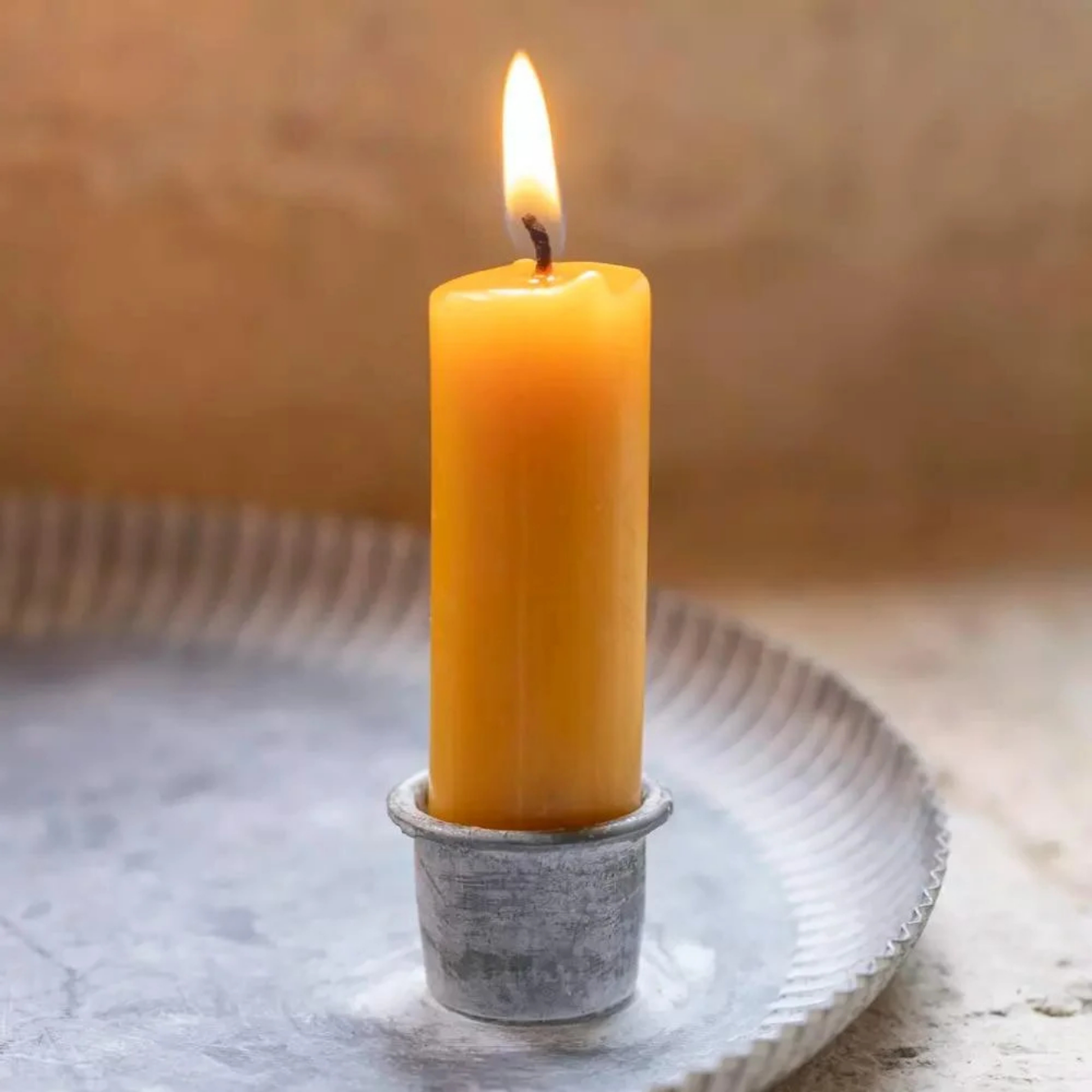 Closeup of metal candle tray holder with a rustic yellow dinner candle