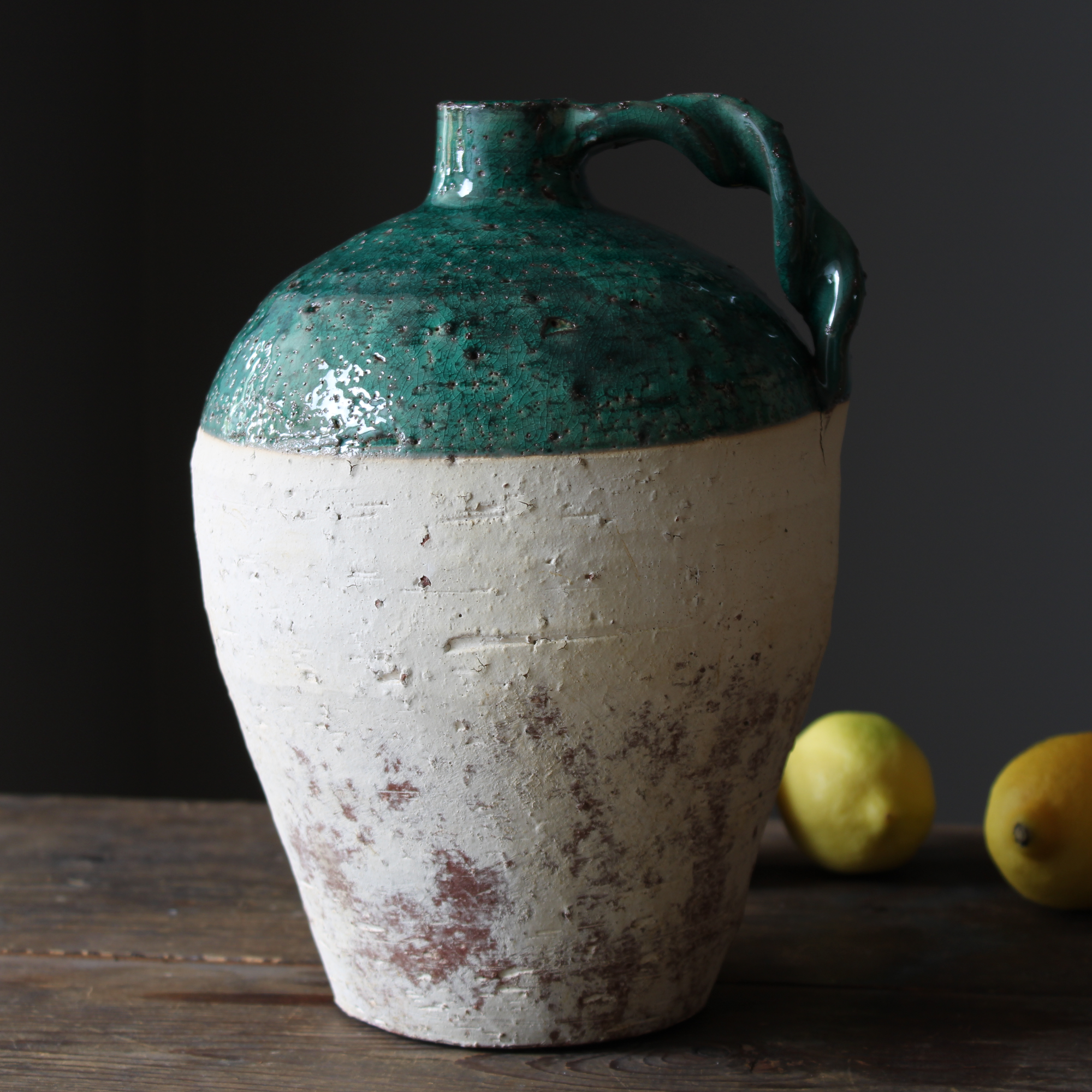 rustic terracotta jug with green glaze on a dark wood kitchen counter, next to lemons.