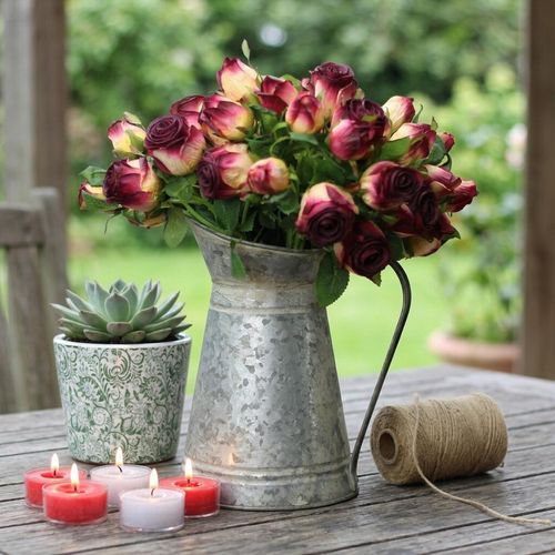 Rustic metal jug with vintage roses on a table