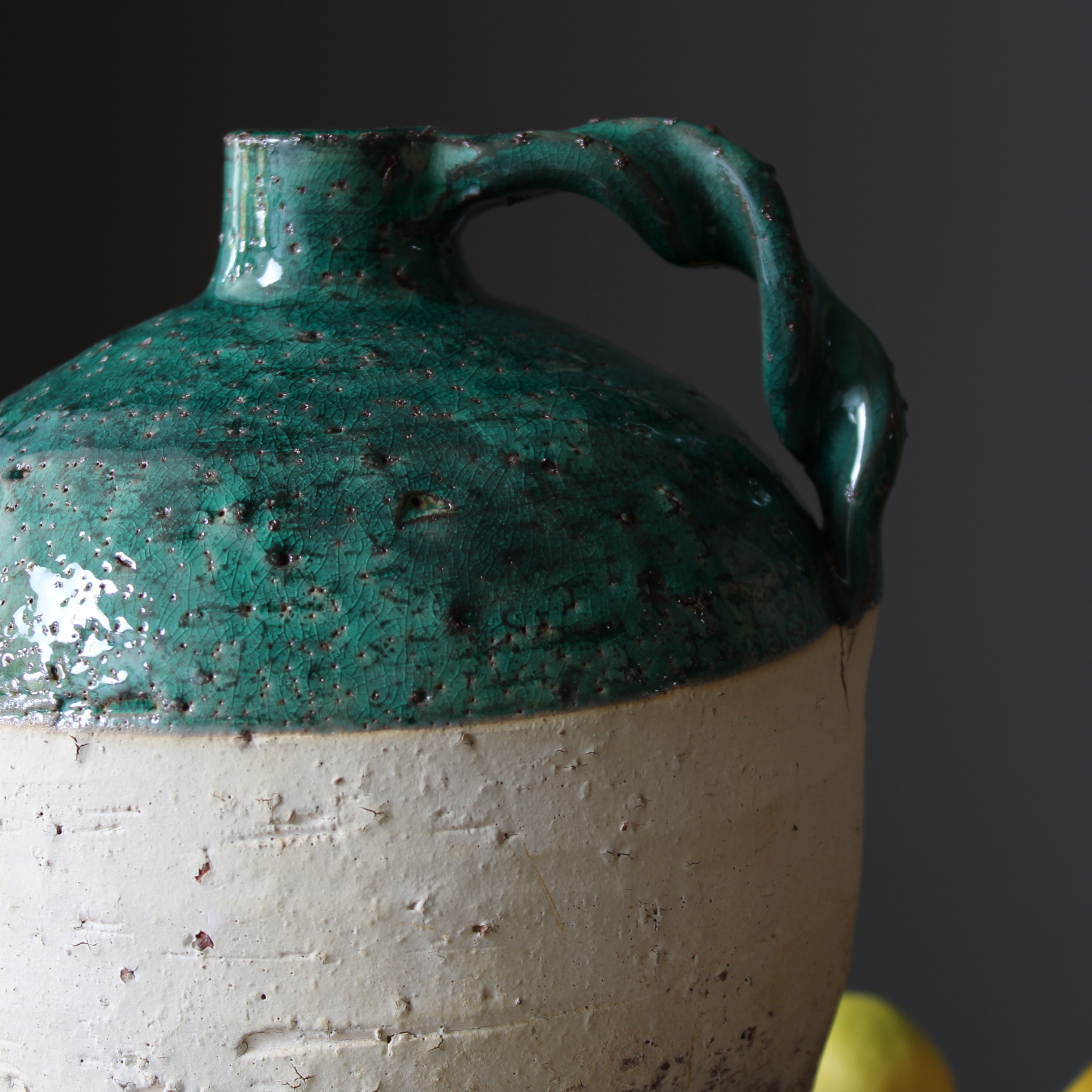 close-up of the speckled green glaze and arched handle of the terracotta jug.