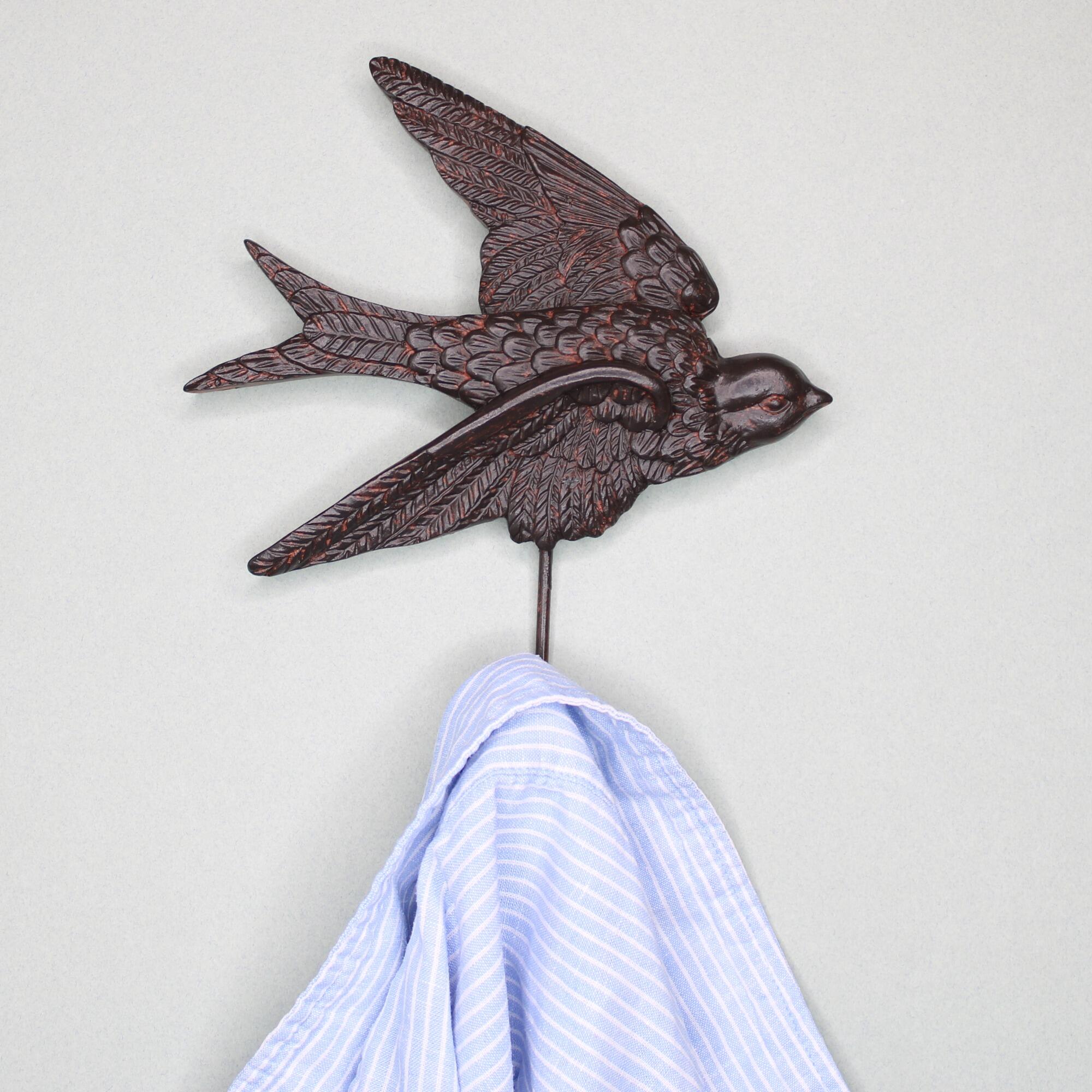 Close-up of an antique bronze swallow wall hook holding a blue and white striped button-down shirt.