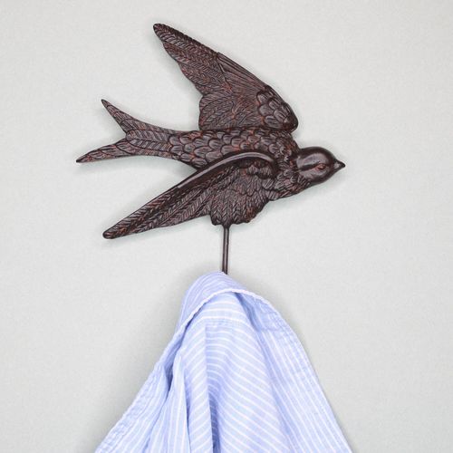 Close-up of an antique bronze swallow wall hook holding a blue and white striped button-down shirt.