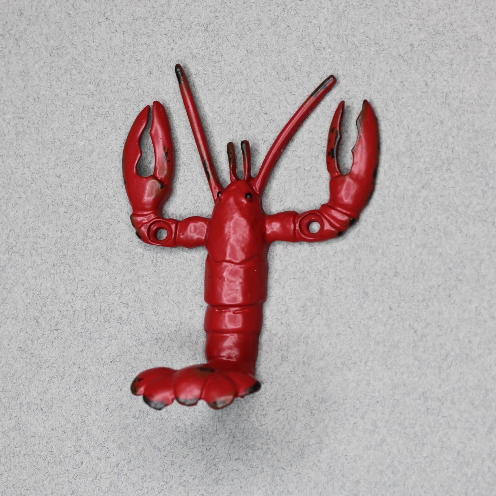 Side view of a metal vintage-style red lobster wall hook mounted on a gray wall, showing the lobster's tail curving outward to form a sturdy hanging hook.
