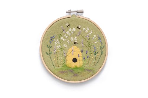 Completed embroidery project in a wooden hoop featuring a 3D yellow felt beehive on an olive green background with embroidered lavender, white flowers, and bees.