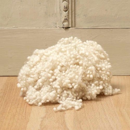 Small pile of natural wool nepps sitting on a wooden table with a rustic sage green cupboard doors behind