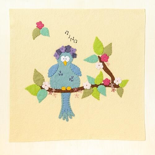 Completed embroidery project featuring a hand-cut blue felt bird with a purple flower crown perched on a brown branch, stitched onto a cream background with embroidered musical notes and pink flowers.