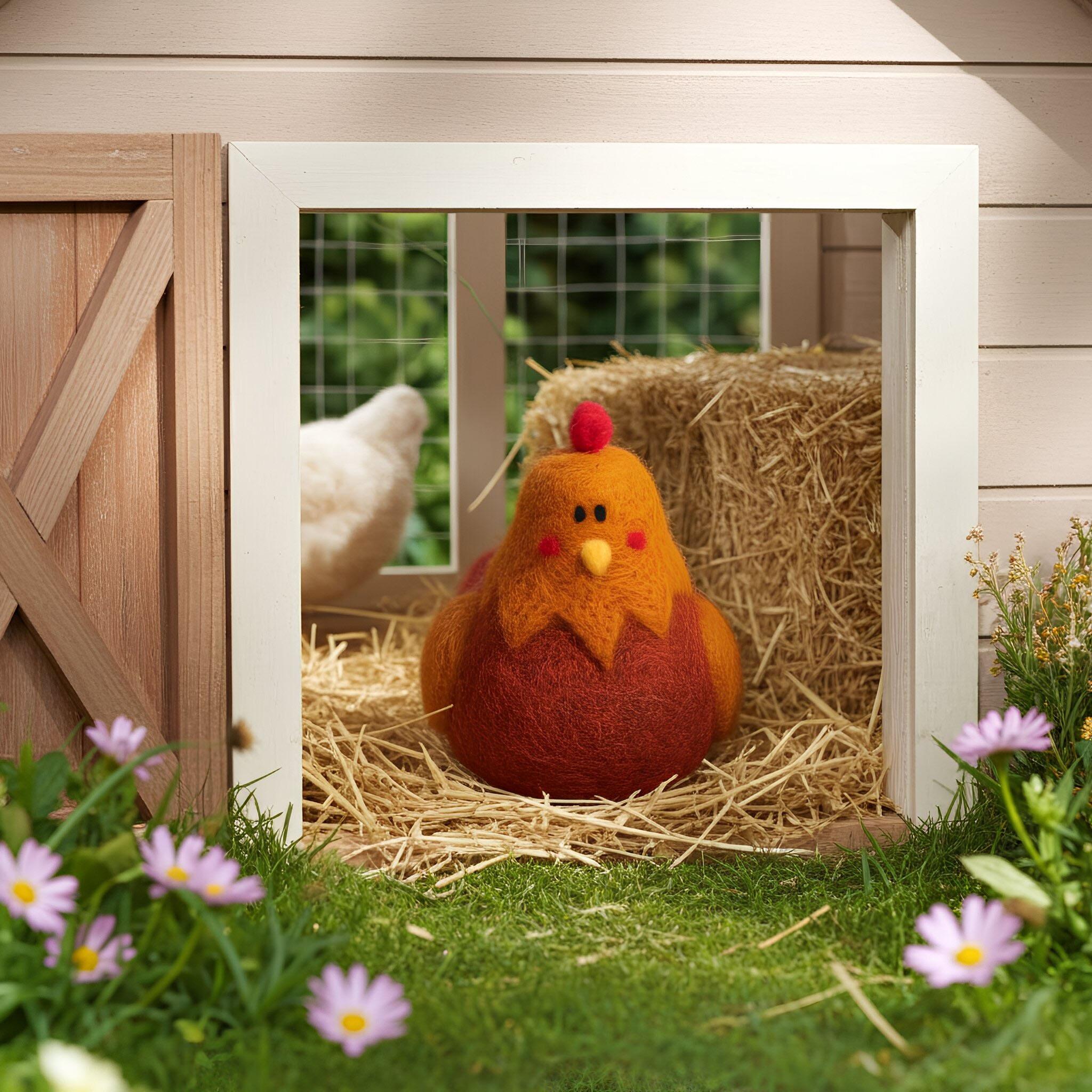A round, orange and red needle-felted chicken with a small red comb and rosy cheeks, sitting on straw inside a light-colored wooden chicken coop, surrounded by spring flowers.
