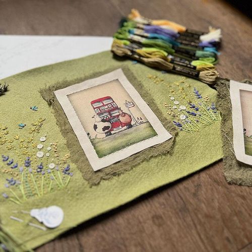 Embroidery kit for the London Bus design, featuring a detailed, stitched scene with a red bus, cows, and delicate flora on green fabric.