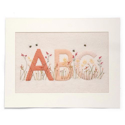 Completed embroidery project featuring felt letters A, B, and C in shades of pink and peach, layered onto a cream felt background with embroidered wildflowers and bees.