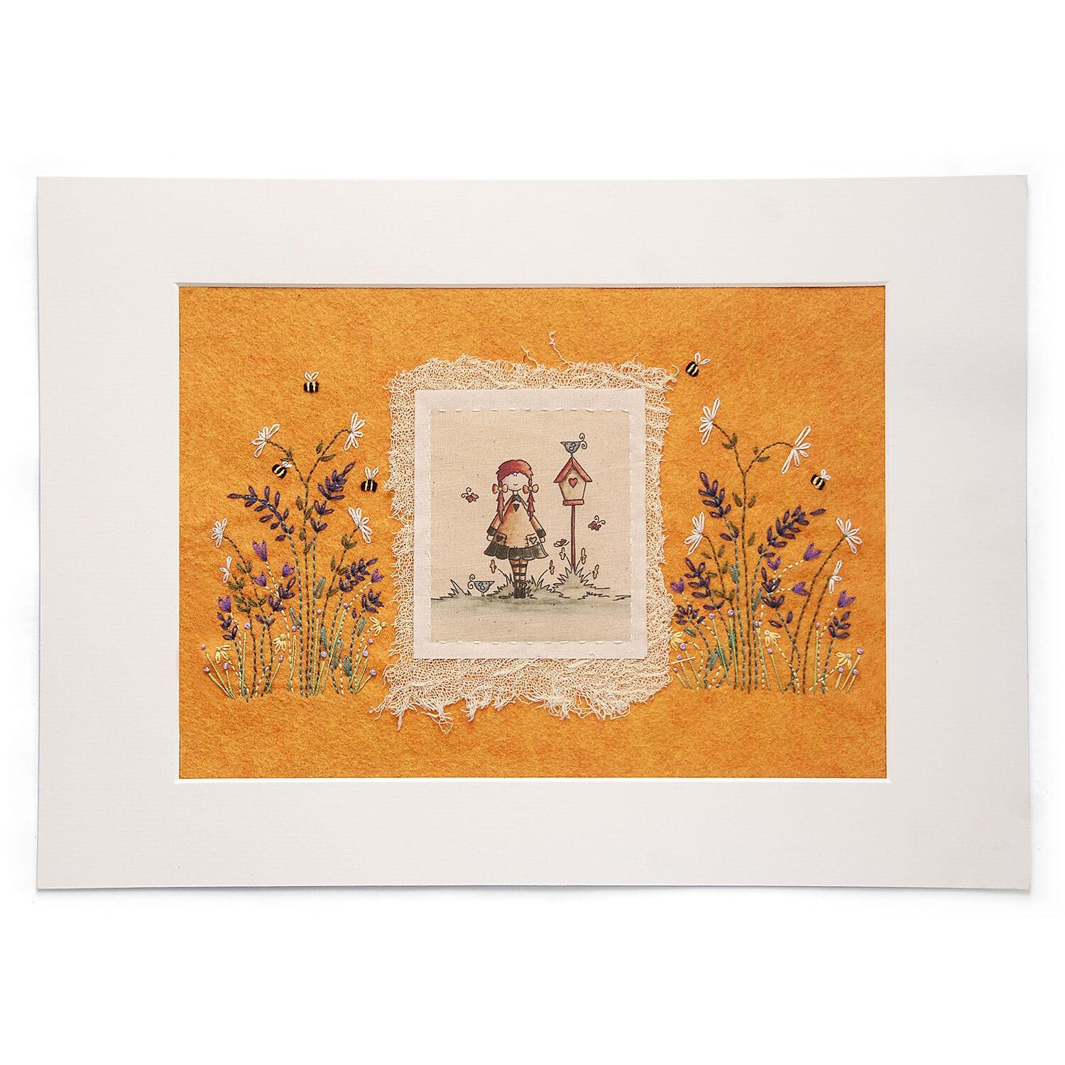 Finished embroidery project featuring a whimsical illustration of a girl named Alexandria standing by a birdhouse, layered onto vibrant orange felt with embroidered lavender, daisies, and bees.