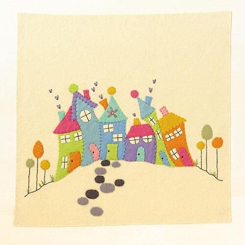 Completed embroidery project featuring hand-cut felt houses in vibrant colors with "wonky" roofs and chimneys, stitched onto a cream felt background with embroidered garden paths and heart-shaped smoke details.