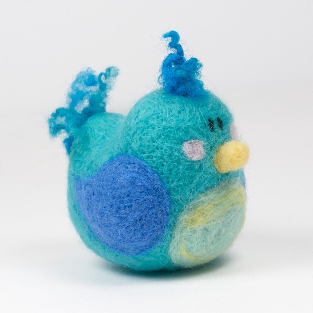 A 3D needle-felted blue bird named Birdie with a turquoise body, bright blue wings, a pale yellow tummy, and curly wool crest and tail.
