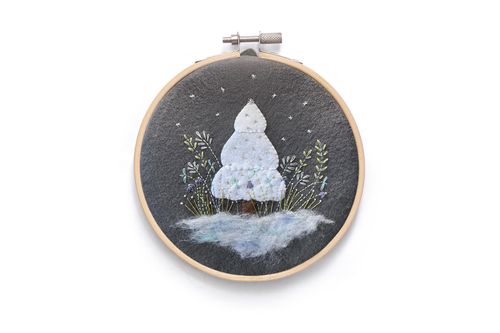 Completed winter embroidery in a wooden hoop featuring a 3D felt white Christmas tree on a dark charcoal background with needle-felted snow and embroidered silver stars.