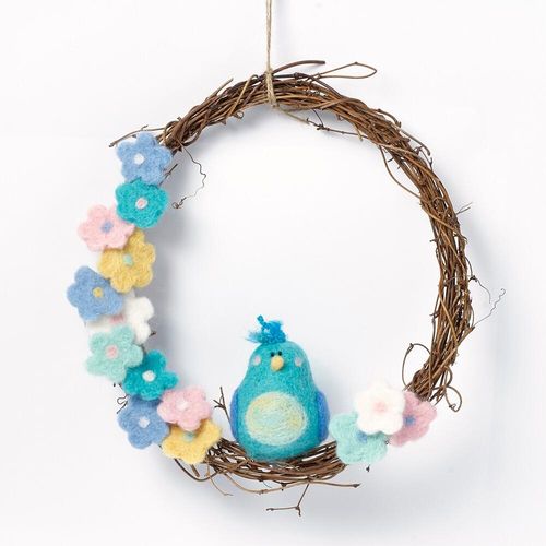 Spring-themed needle felting kit featuring a round twig base, a 3D turquoise birdie with a pale yellow tummy sitting on the bottom rim, surrounded by delicate pink, yellow, and blue felted blossoms.