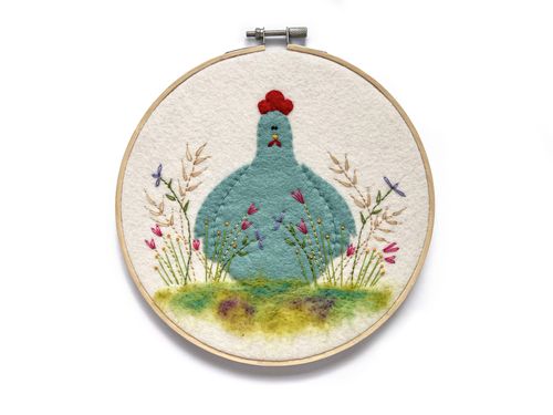 Handmade 'Country Hen' embroidery kit featuring a turquoise felt chicken in a needle-felted wildflower meadow, displayed in a wooden hoop.