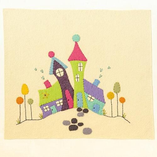 Completed embroidery project featuring a row of four hand-cut felt houses in lime green, teal, purple, and orange with wonky roofs, stitched onto a cream felt background with heart-shaped smoke and stone path details.