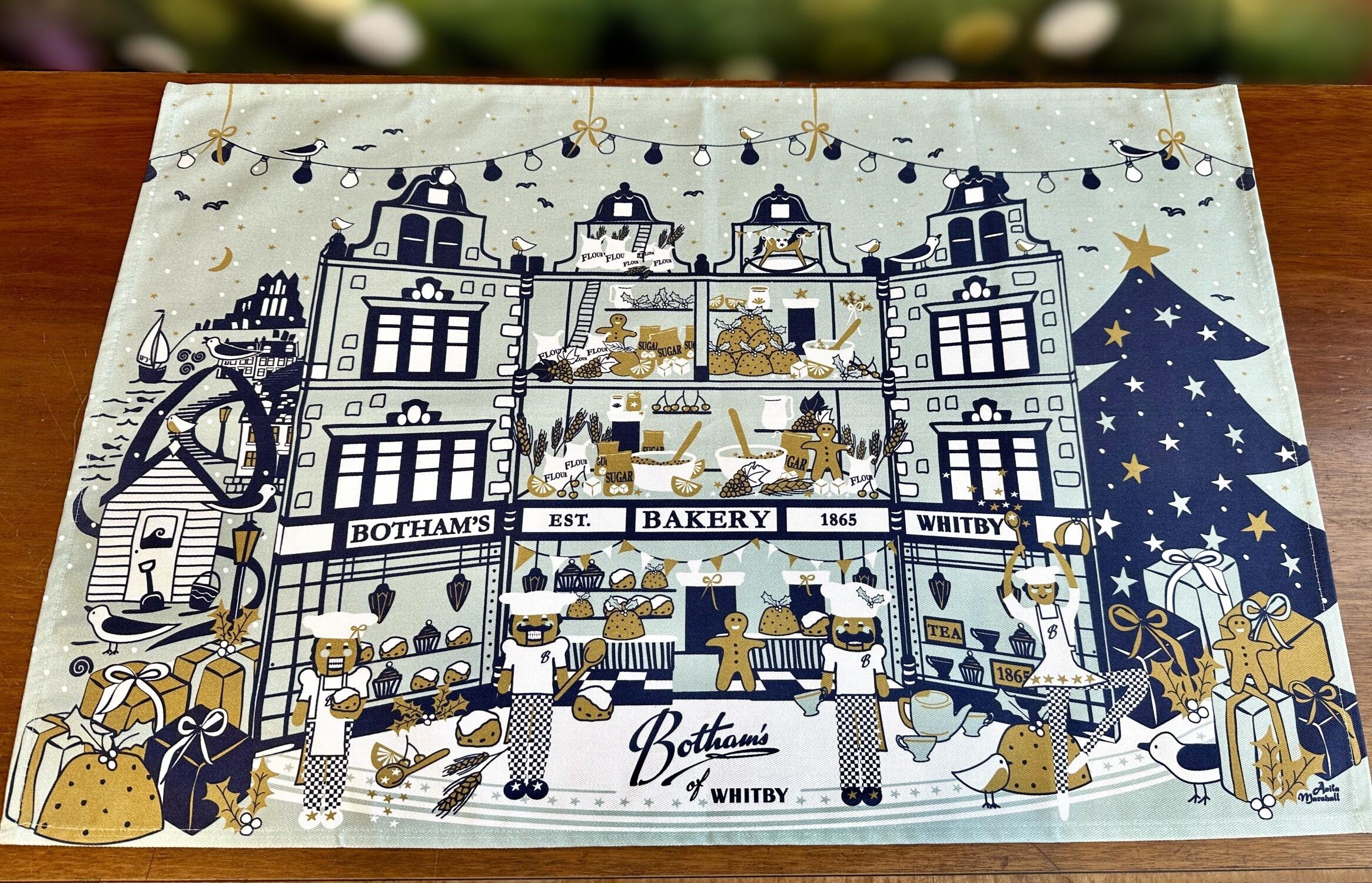 Botham’s of Whitby 2025 Christmas Tea Towel by family designer, Anita Marshall. This year’s design depicts a magical interpretation of a Botham’s Nutcracker scene, featuring the historical Skinner Street Shop and bakery, Nutcracker bakers, Christmas tree, Whitby’s Whale Bones, the one hundred and ninety=-nine steps and Whitby Abbey. Bespoke baking memorabilia and festive adornments add a unique, festive atmosphere to this tea towel - add some Botham’s magic to your washing up! From Botham’s iconic Whitby bakery with love at Christmas.