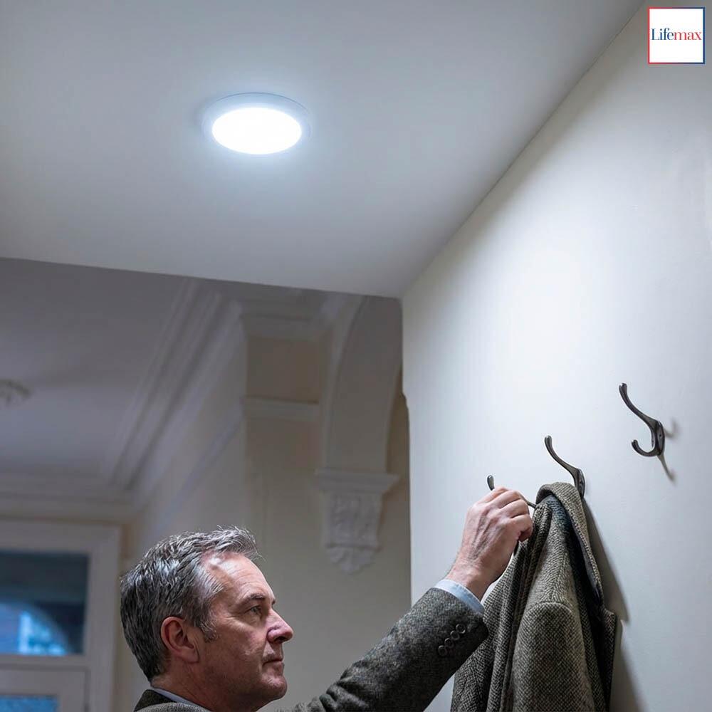 A middleaged man hanging up his coat in a hallway illuminated by the Lifemax Rechargeable Motion Ceiling Light