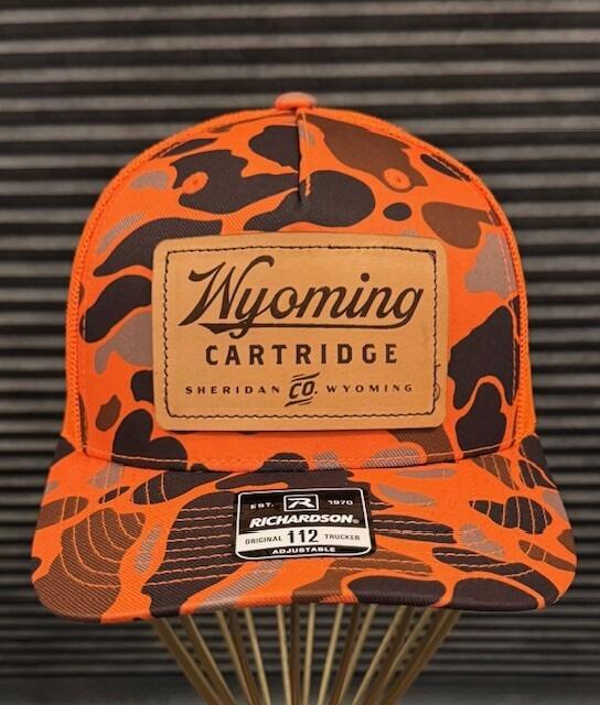 orange camo front panel and bill with a brown badge with Wyoming Cartridge Company logo centered on panel