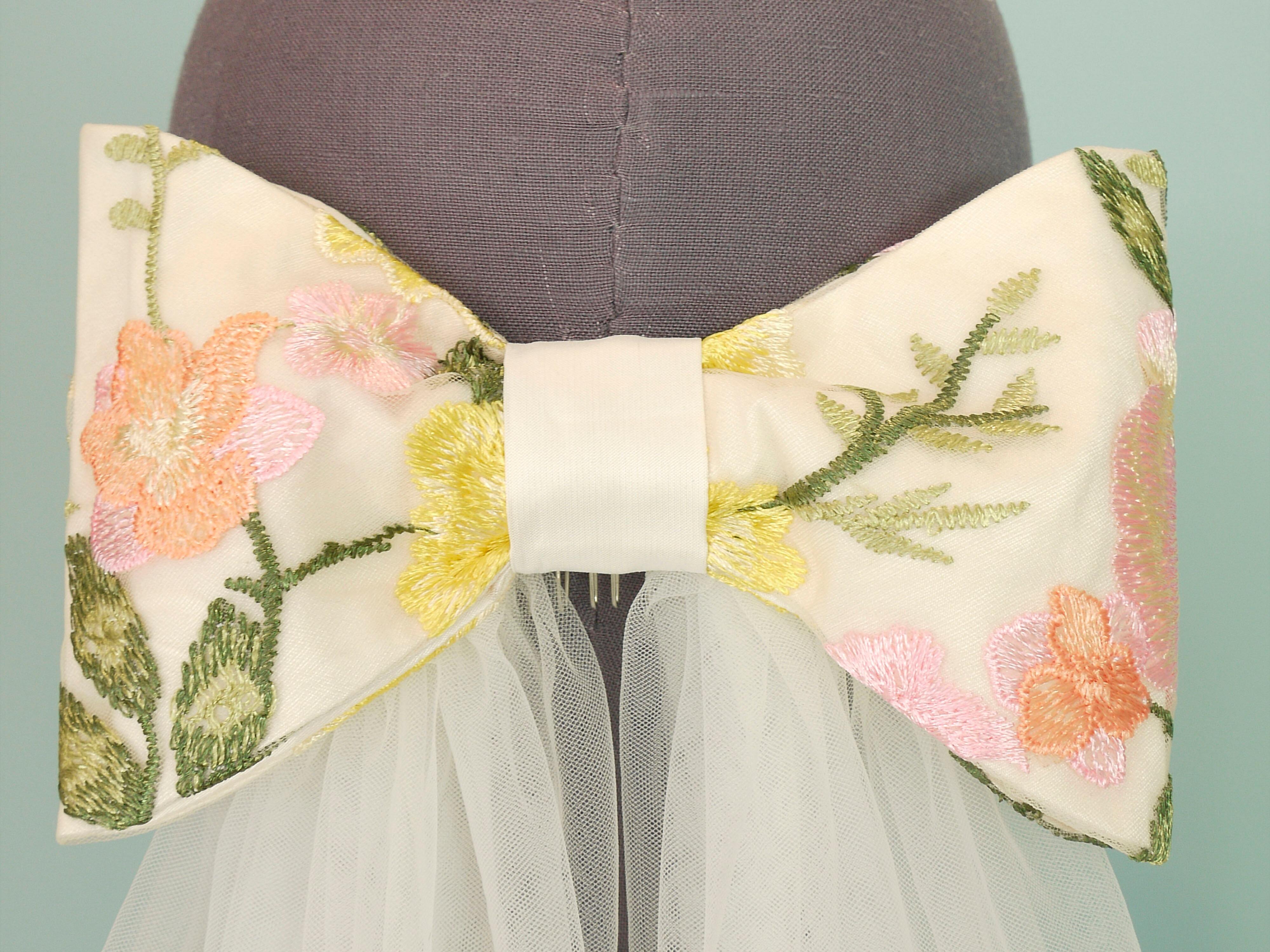 A bridal bow hair accessory made in silk and floral lace with soft tulle tails