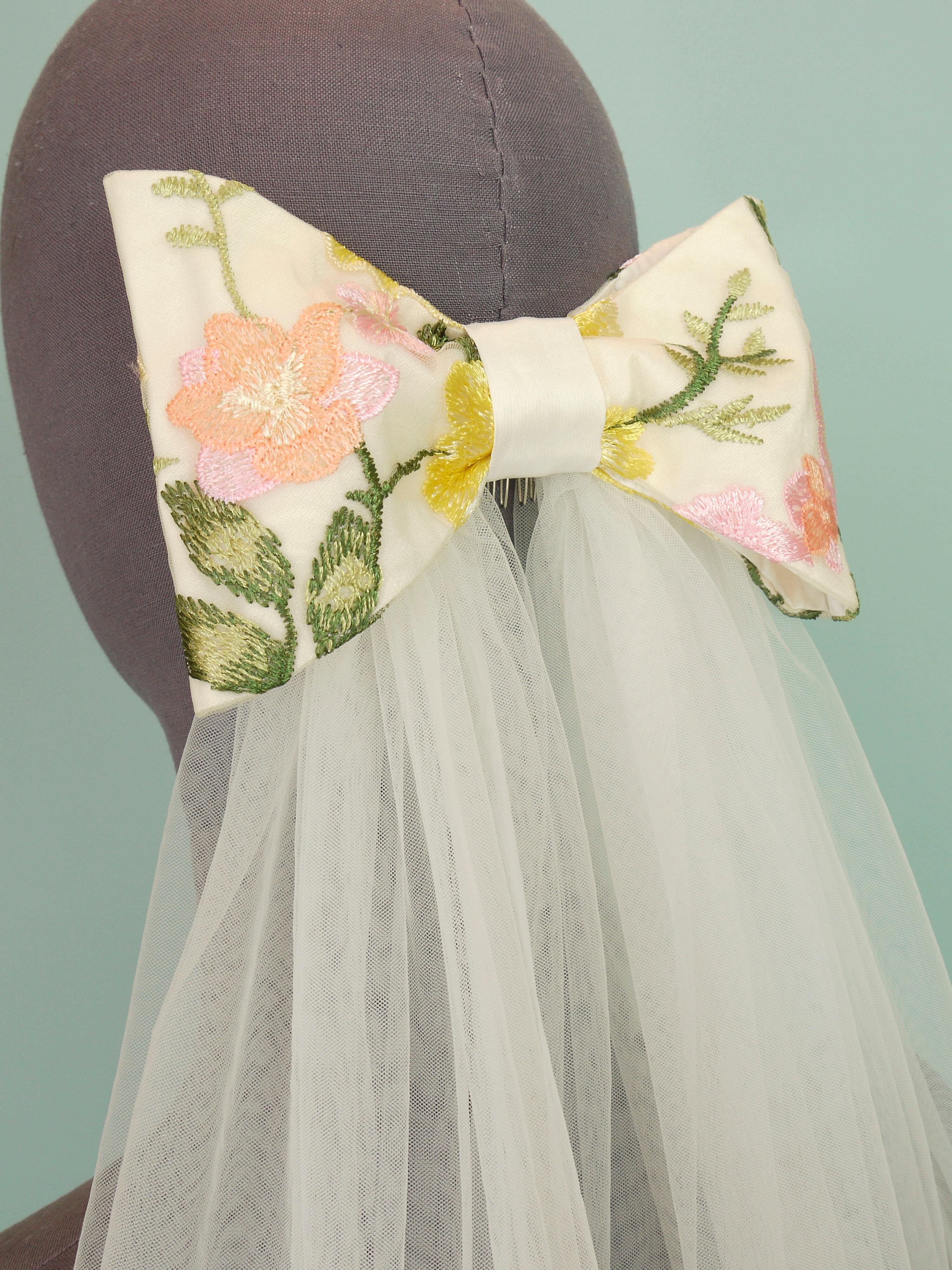 A bridal bow hair accessory made in silk and floral lace with soft tulle tails
