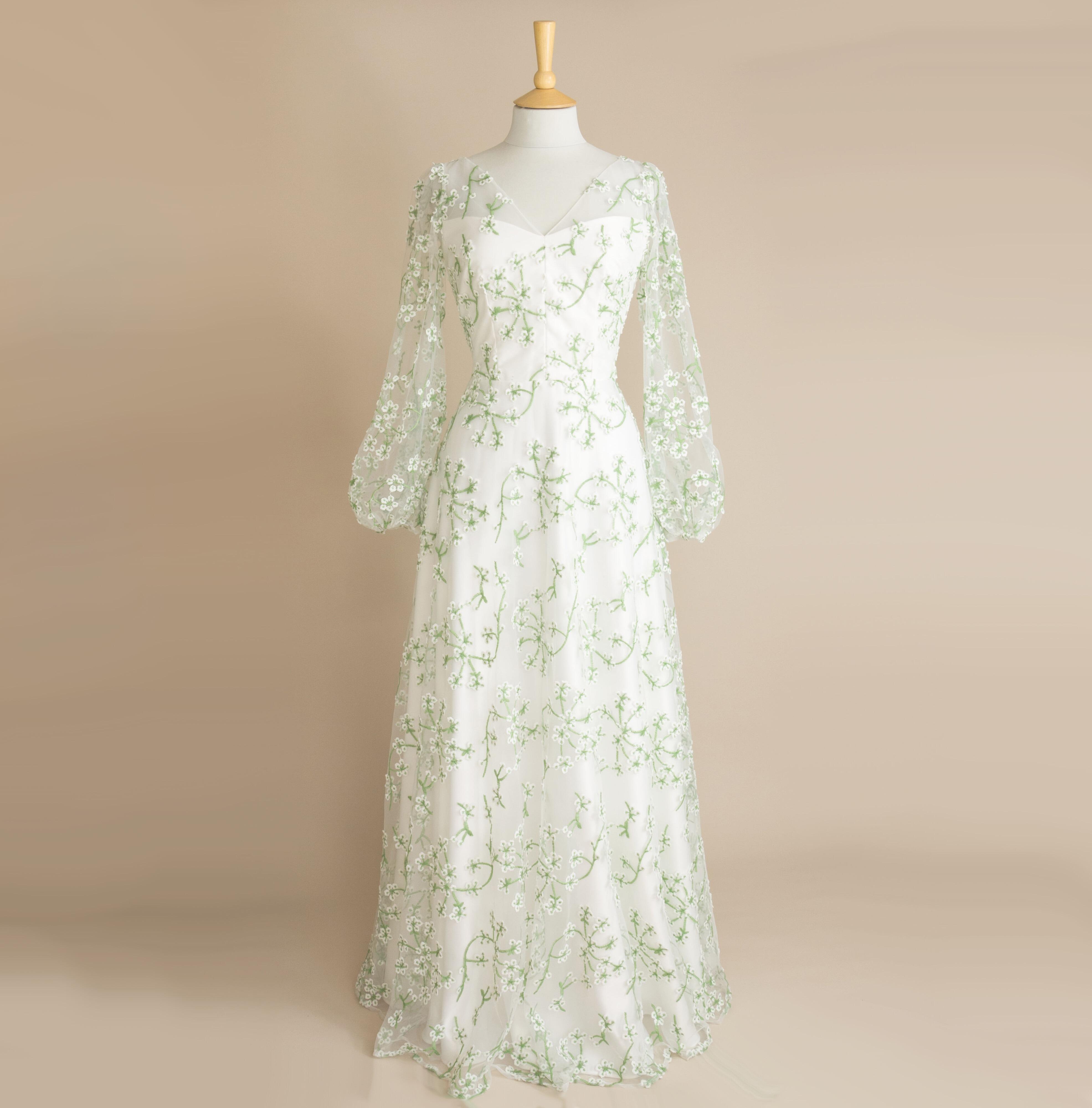 a green floral lace wedding dress with long lace sleeves on a plain background