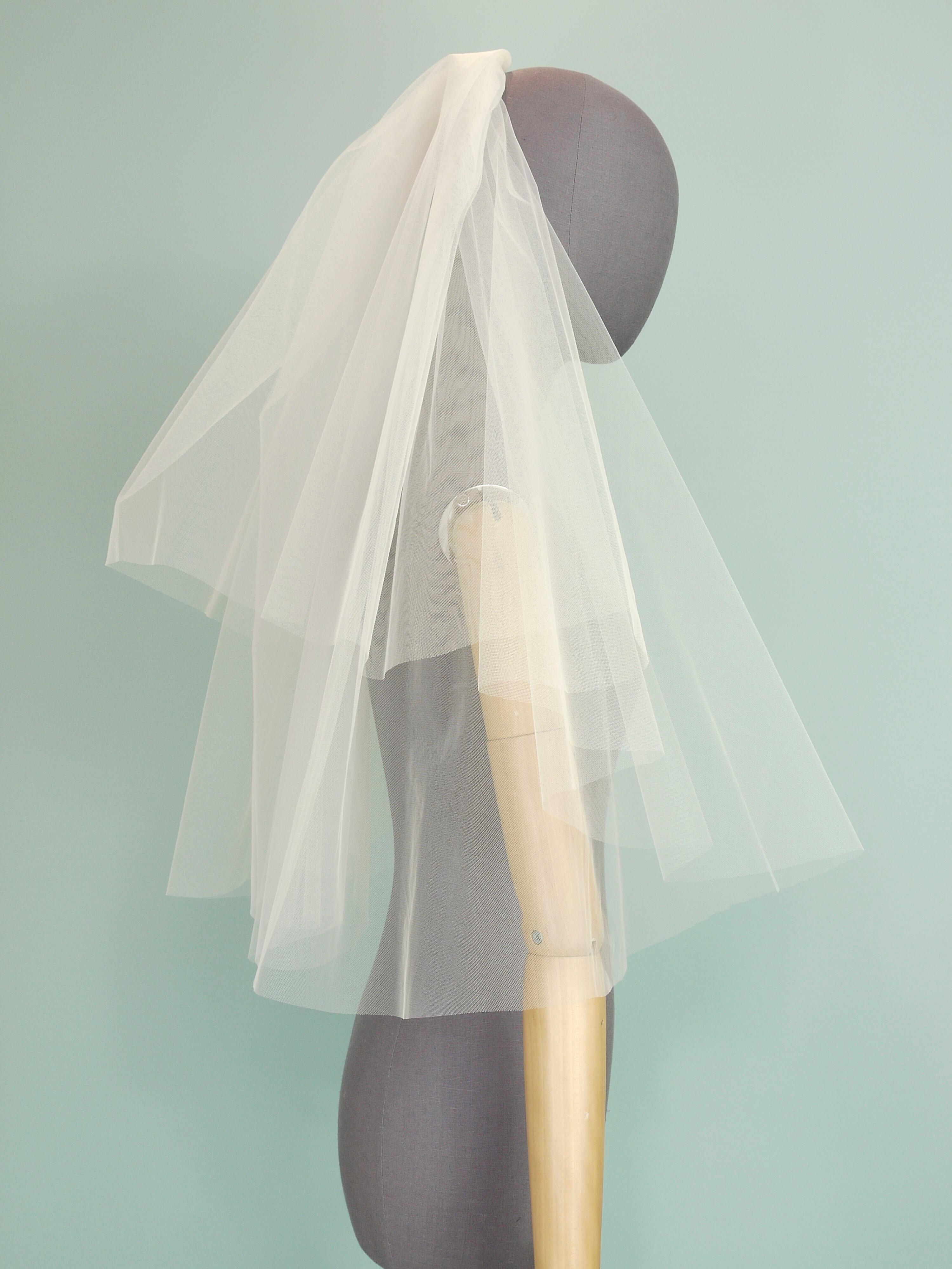 An ivory tulle wedding veil with a tiered shape on a grey mannequin