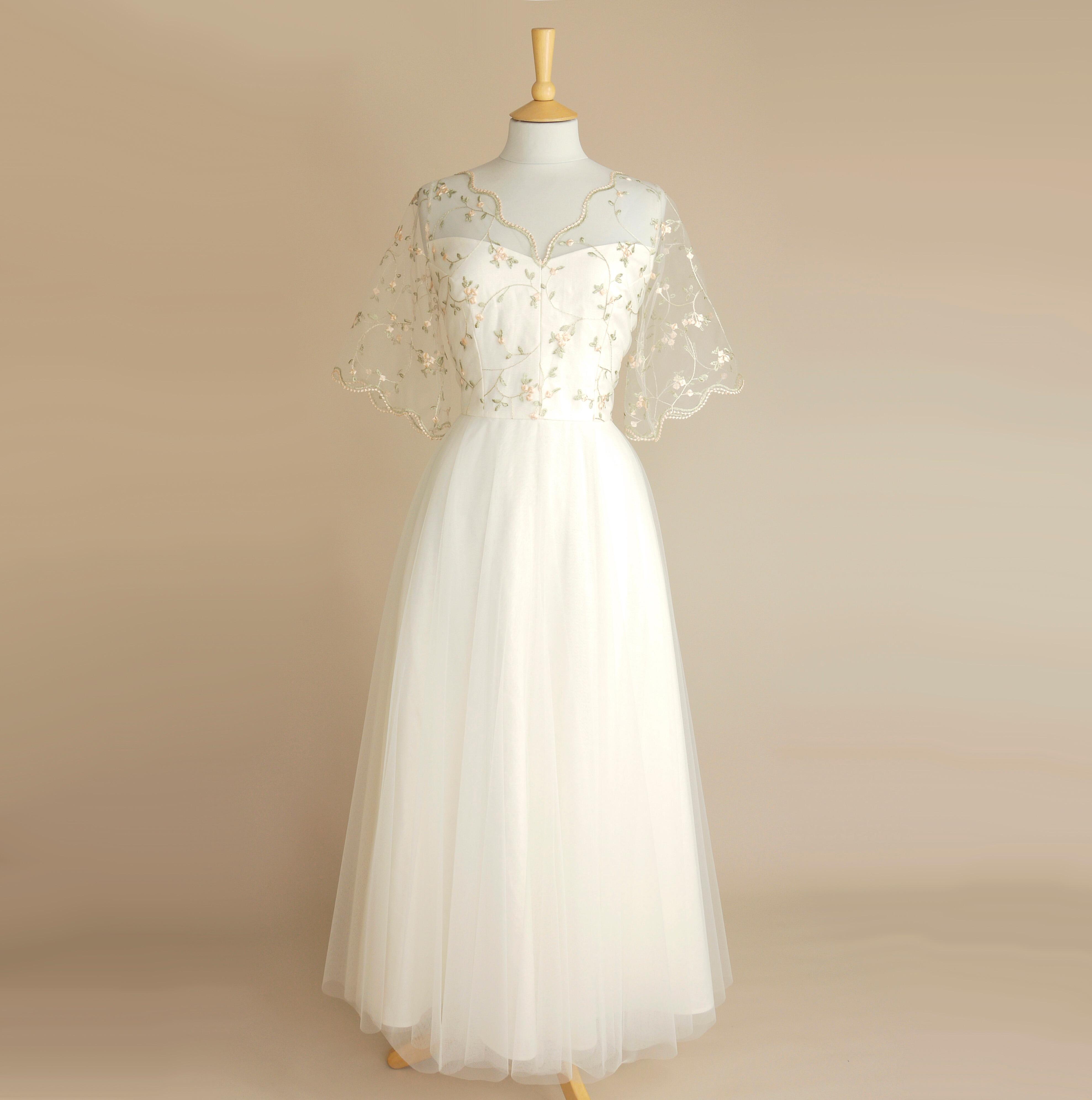 an exquisite vintage style wedding dress in ivory linen, soft tulle and a delicate apple blossom lace shown on a plain background