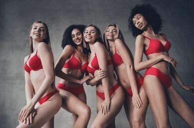 Five women wearing red lingerie standing side by side against a grey background, showcasing a range of sizes and styles.