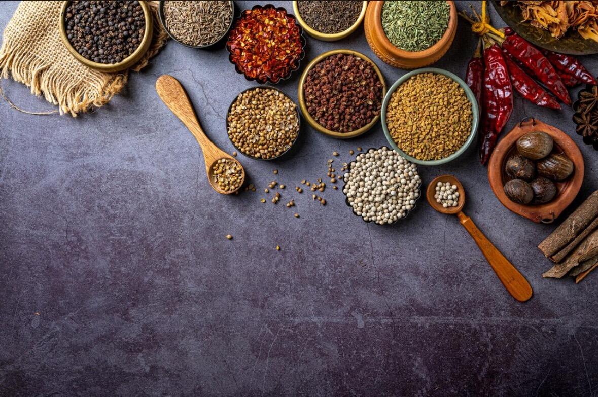 Several small bowls filled with colorful spices including turmeric, paprika, and cumin, arranged on a grey worktop.