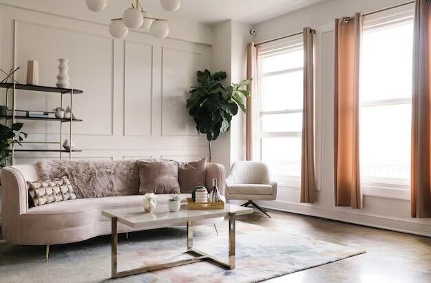 Very light pink sofa centered in a cream-coloured living room with soft, neutral décor