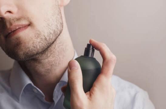 White male holding a dark-colored fragrance bottle, spraying cologne on himself, showcasing men’s luxury perfume application.