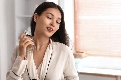 Woman holding a glass fragrance bottle, spraying perfume on her neck, showcasing elegant women’s luxury fragrance application.