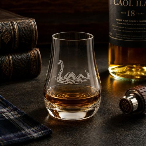 Loch Ness Monster engraved whisky tasting glass with Scotch whisky in a rustic distillery setting