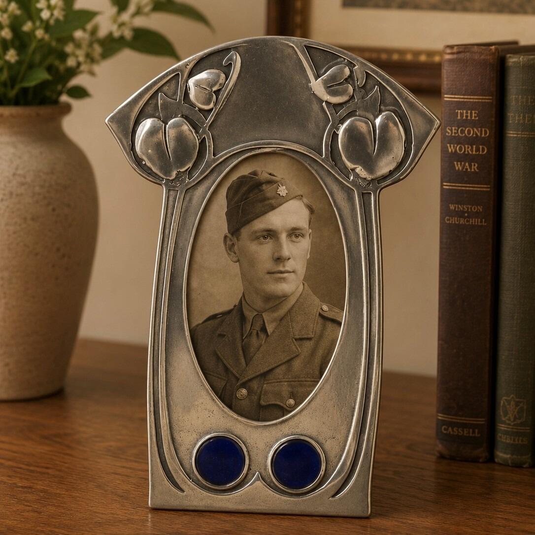 An Art Nouveau Liberty style pewter picture frame with a stylized leaf design and two round blue enamel inserts, displaying a vintage black and white photograph of a man in a WWII military uniform
