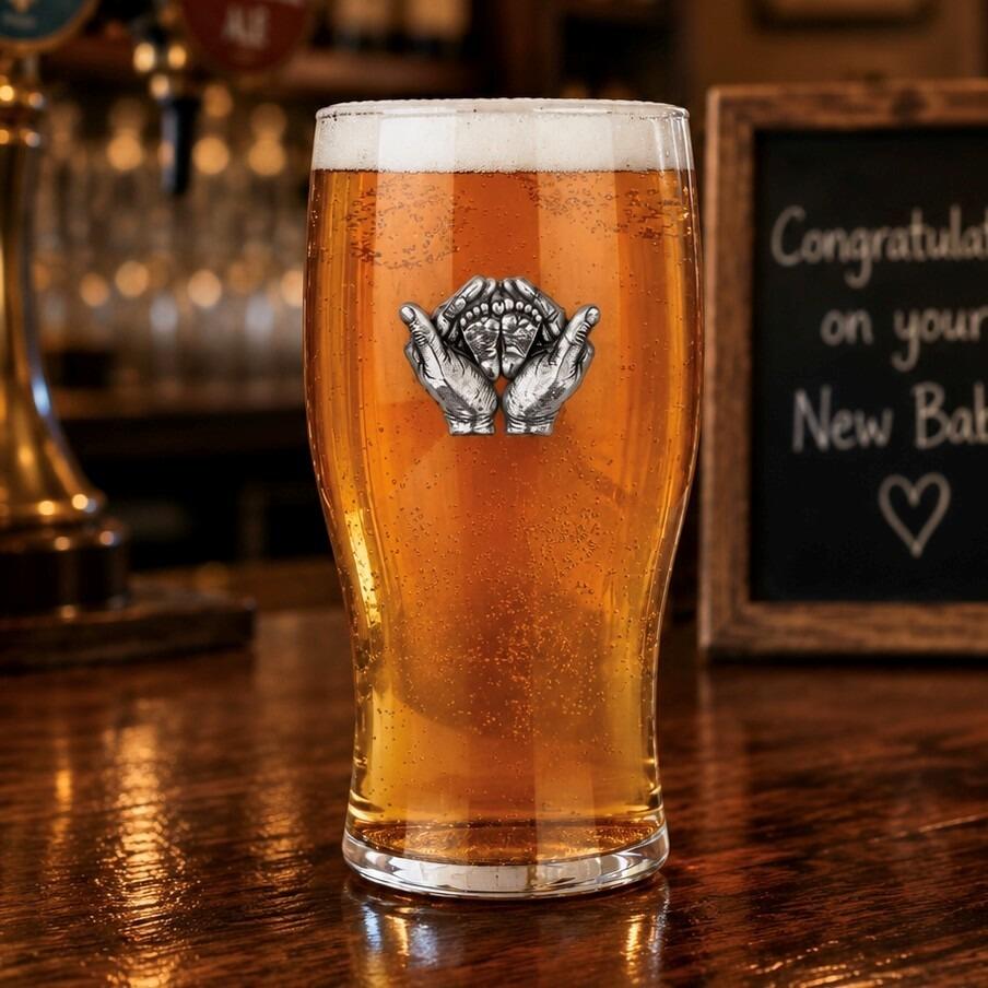 Pint glass with handmade pewter “New Baby” badge, filled with golden beer