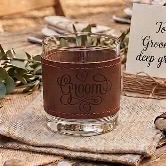 Glass tumbler wrapped in a brown stitched leather sleeve engraved with the word "Groom" and a small heart
