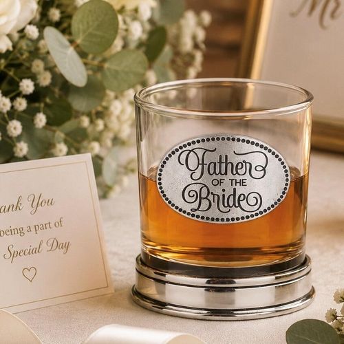 Whisky tumbler with pewter 'Father of the Bride' badge and polished base, partially filled with amber liquid