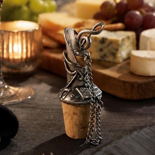 Pewter wine pourer and cork stopper featuring a sculpted treble clef top and engraved musical notes, displayed on a table beside a cheese board and a lit candle