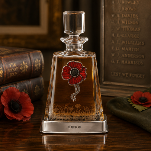 A clear glass spirits decanter filled with golden-amber liquid, sitting in a smooth pewter base detailed with stamped hallmarks. The front of the decanter is adorned with a large pewter emblem of a stylized poppy flower with red enamelled petals and a black centre, curving down into a textured stem