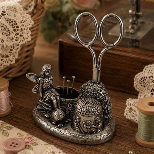 Vintage-style pewter fairy sewing station featuring a seated fairy figurine, a textured bush scissor holder, a floral thimble stand, and a small round pincushion