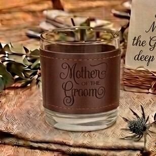 Glass tumbler wrapped in a brown stitched leather sleeve engraved with the words "Mother of the Groom" in elegant script