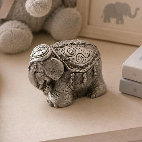 Pewter keepsake box intricately sculpted into the shape of a decorated elephant wearing an ornate ceremonial saddle blanket with tassels, displayed on a table with nursery decor