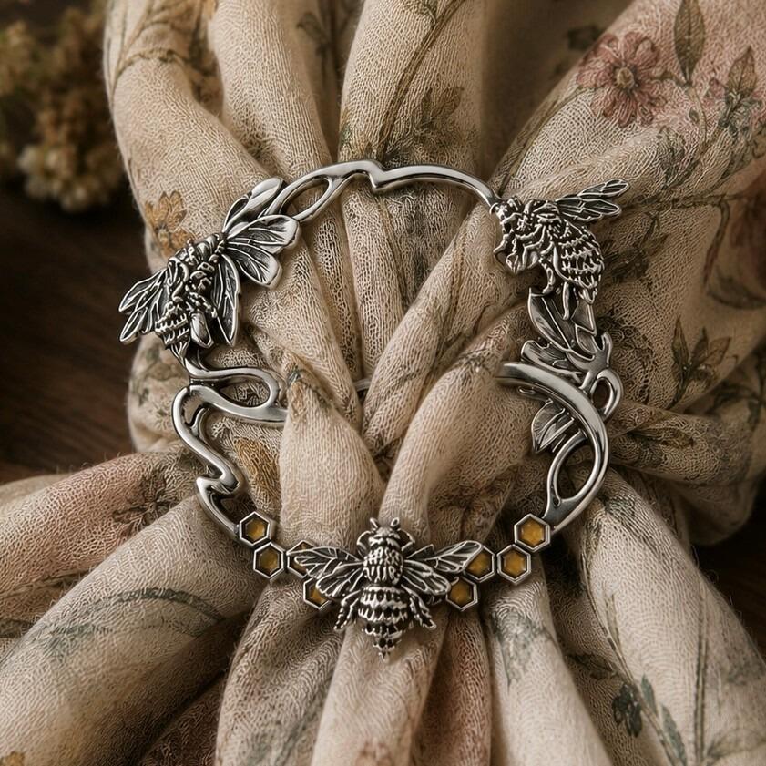 Circular pewter scarf ring featuring detailed honeybees and amber-tinted honeycomb accents, cinching a floral patterned fabric scarf
