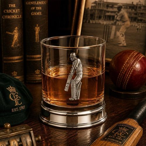 Whisky tumbler with pewter cricket player emblem and polished base, partially filled with amber liquid